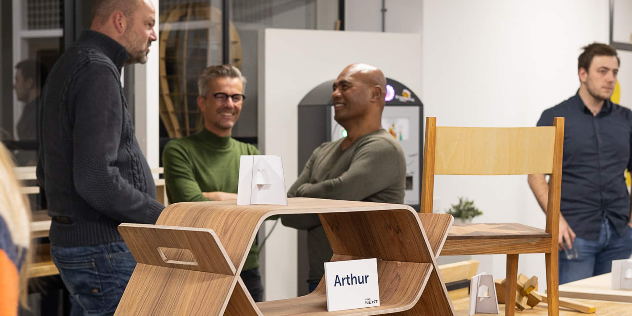 Drie mannen staan om een handgemaakt meubelstuk op de eindexpositie van de training meubelmaken basis bij Cibap Next in Cibap vakschool voor vormgeving in Zwolle