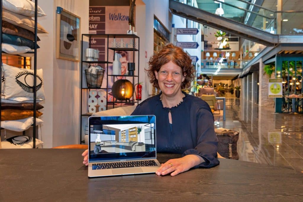 Hennie Kapenga zit achter een computer waarop ze een interieurontwerp in SketchUp Pro toont. De vrouw zit aan een tafel in een interieurzaak.
