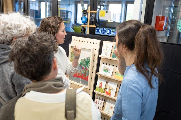 Katja Kaduk toont haar eindwerkstuk, een houten meubelstuk wat dient als kaartenrek, aan een groep mensen. Het meubelstuk staat op de eindexpositie van de training meubelmaken van Cibap Next op Cibap vakschool in Zwolle.