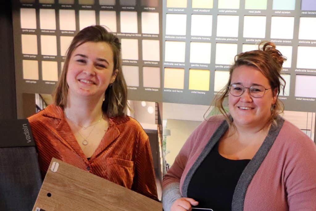 Twee medewerkers van Woonstudio Raalte met verf en hout in hun handen voor een rek met kleurenstalen